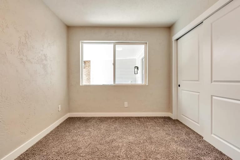 Bedroom addition with textured walls, carpet, sliding-door closet, and natural light from interior window — Utah bedroom addition by CasaMás Construction