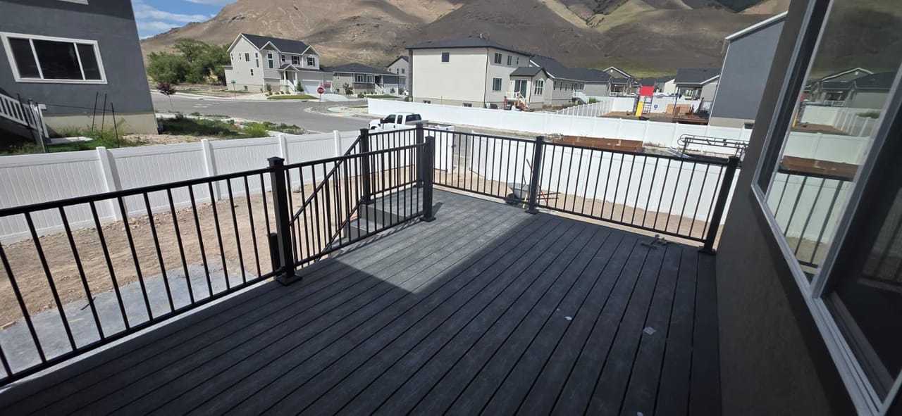 Deck de composite gris con barandal negro con vista a barrio suburbano de Utah y montañas al fondo, en etapa de construcción — por CasaMás Construction