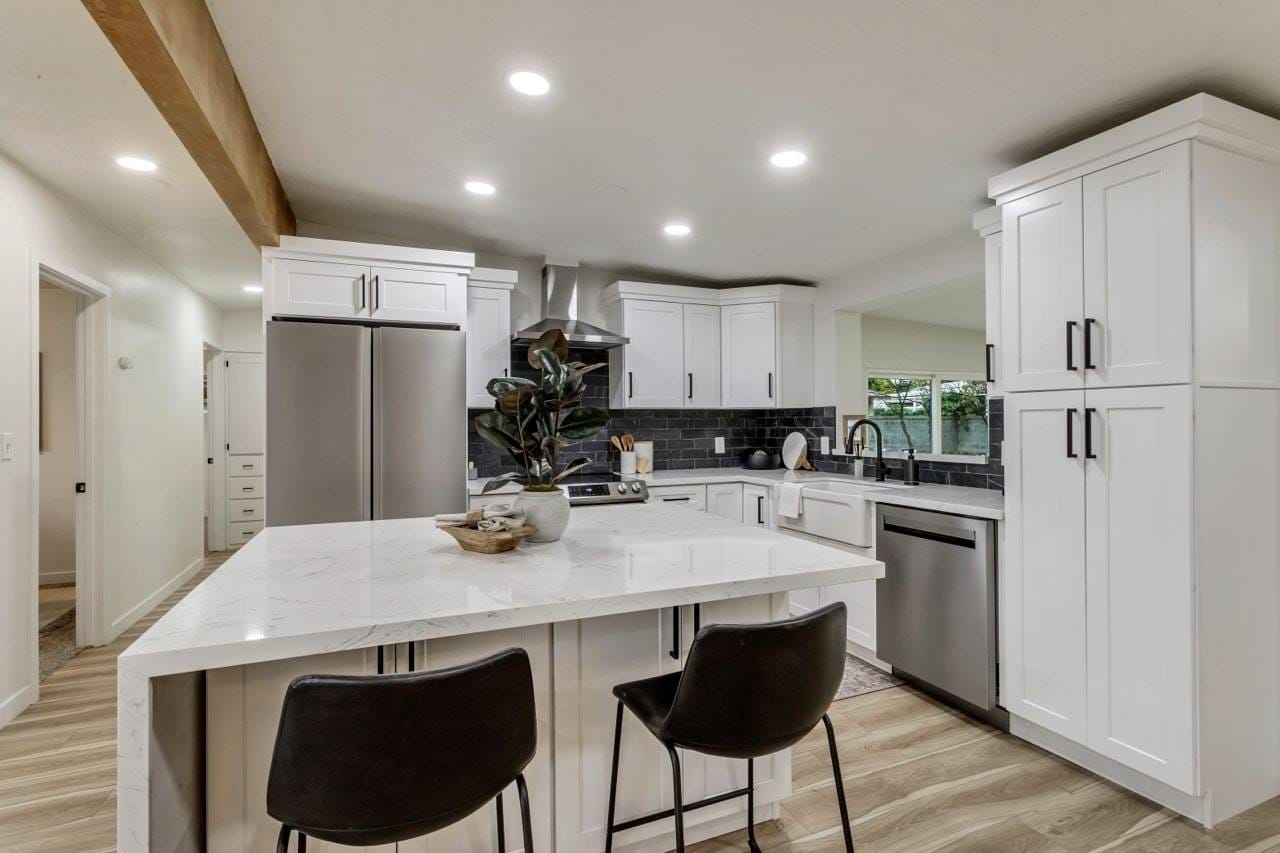 White shaker kitchen with dark subway-tile backsplash, marble waterfall island, stainless appliances, and black hardware — Utah kitchen addition by CasaMás Construction