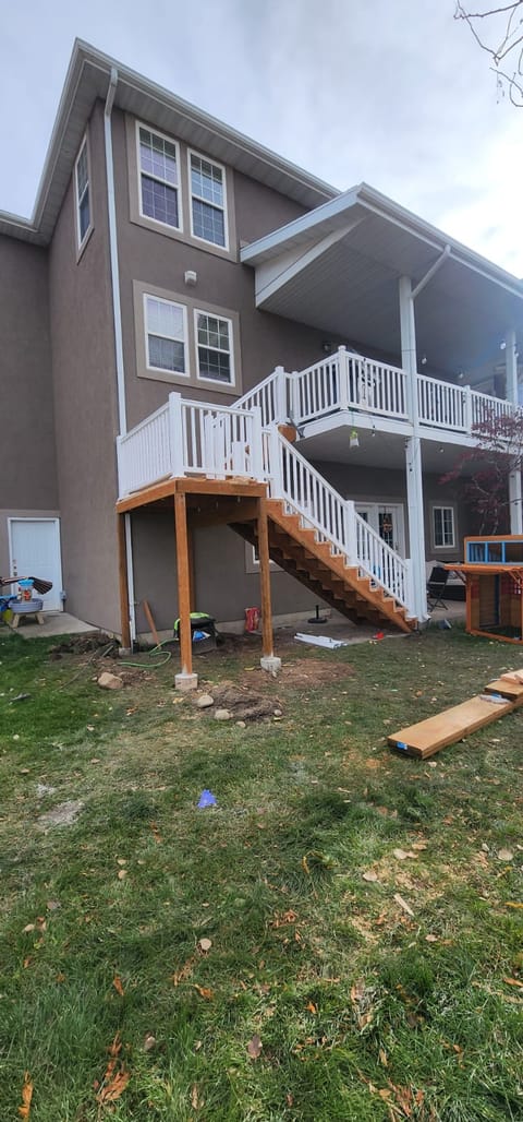 Sistema de deck de dos pisos con barandales blancos y escaleras de madera conectando los niveles en casa de estuco — deck de dos pisos en Utah por CasaMás Construction